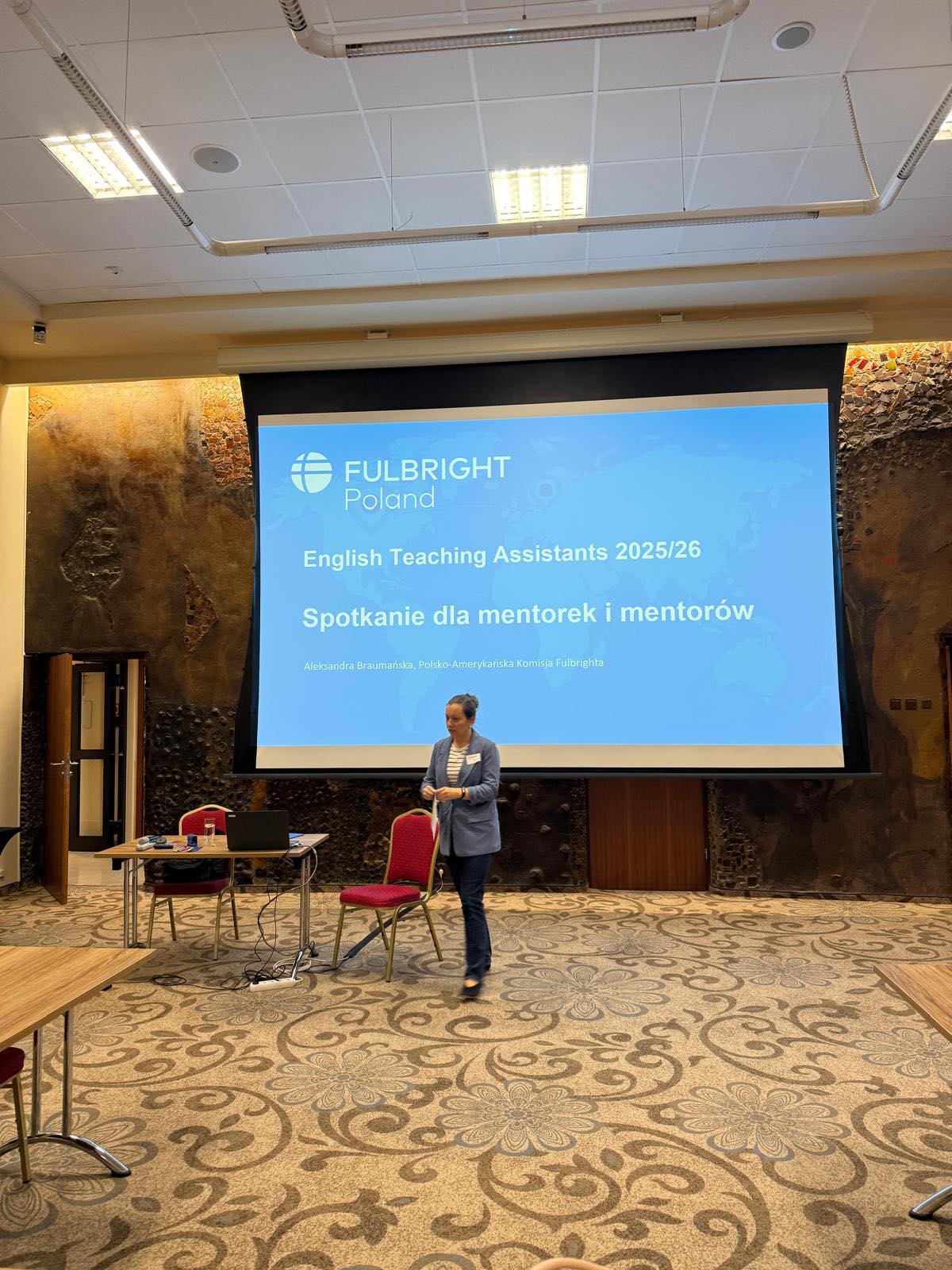 Przedstawiciel Komisji Fulbright w sali rozpoczynający spotkanie mentorów i mentorek. W tle ekran z prezentacją.